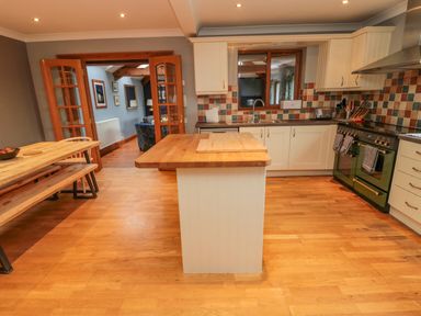 A kitchen with wooden flooring an island central table a dining table with bench seating and a doorway opening to another room at Ridley Lodge in West Thirston felton