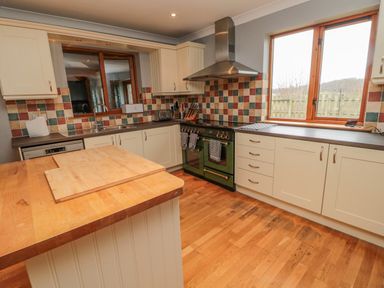 A kitchen with wooden floors a central wooden island cooker with extractor and window at Ridley Lodge West Thirston felton