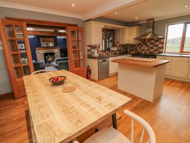 A kitchen with an island wooden dining table and chairs visible through glass doors at Ridley Lodge in West Thirston felton