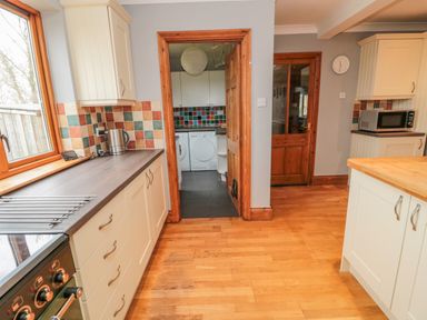A kitchen with wooden floors, white cabinets, a kettle, a microwave, and a laundry room visible through a doorway at Ridley Lodge in West Thirston felton