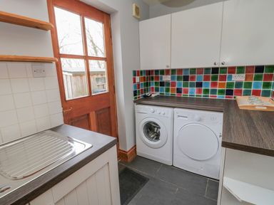 A laundry room with washing machine and dryer under countertop near wooden door and colorful tiled backsplash at Ridley Lodge in West Thirston felton