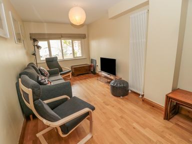 A living room with chairs a sofa a television and a wooden floor at Ridley Lodge in West Thirston felton