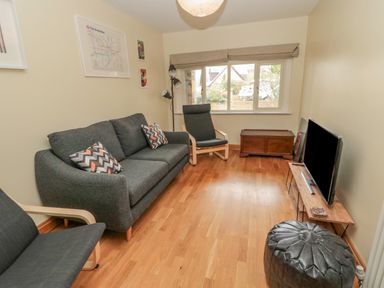 A small living room with a gray sofa and chair a wooden floor a television on a stand and a window at Ridley Lodge in West Thirston felton