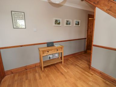 A hallway with wooden flooring a small wooden table and framed pictures on the wall at Ridley Lodge in West Thirston felton