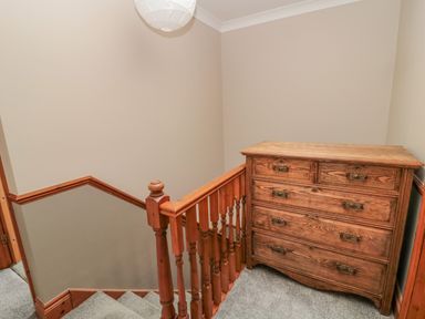 A staircase landing with a wooden chest of drawers and carpeted floor at Ridley Lodge in West Thirston felton