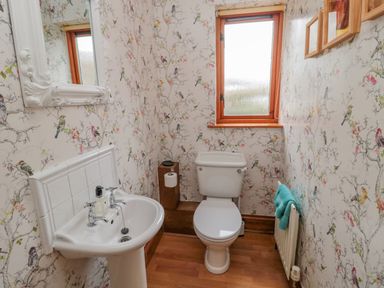 A bathroom with a white toilet pedestal sink a mirror a radiator with a towel and bird patterned wallpaper at Ridley Lodge West Thirston felton