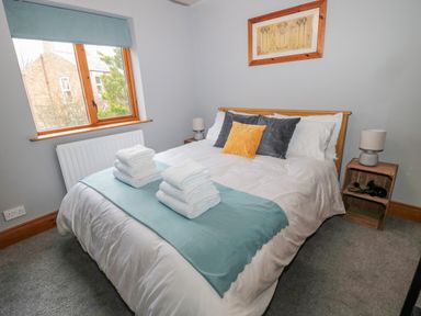 A bedroom with a double bed white linens folded towels on bed bedside tables with lamps and window at Ridley Lodge in West Thirston/felton