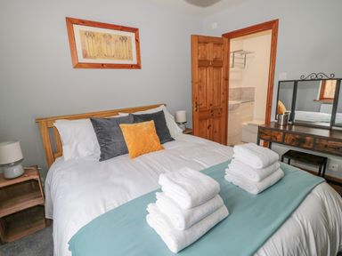 A bedroom with a made bed with towels on it and a wooden dresser with a mirror at Ridley Lodge in West Thirston felton