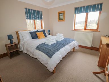 A bedroom with a bed set with folded towels bedside tables with lamps and two windows at Ridley Lodge in West Thirston felton