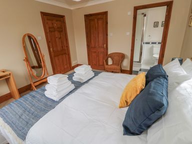 A bedroom with a bed with folded towels and pillows a wicker chair a full length mirror and wooden doors at Ridley Lodge in West Thirston felton