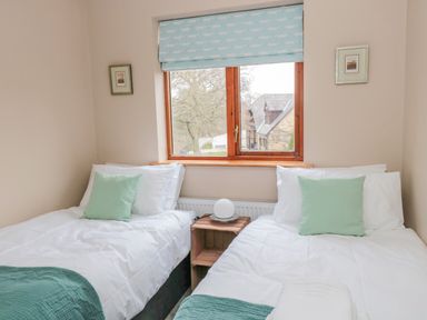 A bedroom with two single beds and a window between them at Ridley Lodge in West Thirston felton
