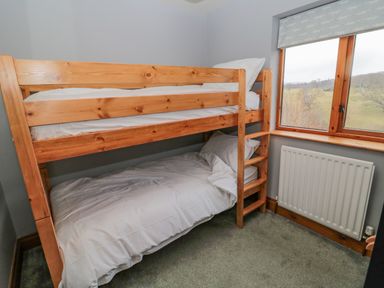 A bedroom with wooden bunk beds next to a window with a view of trees at Ridley Lodge in West Thirston felton