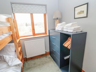 A small bedroom with a wooden bunk bed near a window and a dark dresser with folded towels and hangers at Ridley Lodge in West Thirston felton