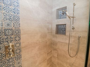 A shower with patterned blue tiles built into niches and a handheld showerhead at Ridley Lodge West Thirston felton