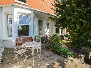A patio area with white metal table and chairs a wooden bench and greenery at Florence Villas in Worcester