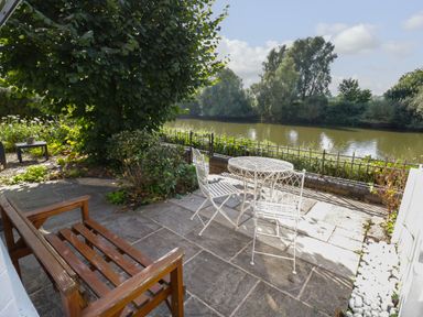 An outdoor patio with a wooden bench and white metal table and chairs by a river at Florence Villas in Worcester
