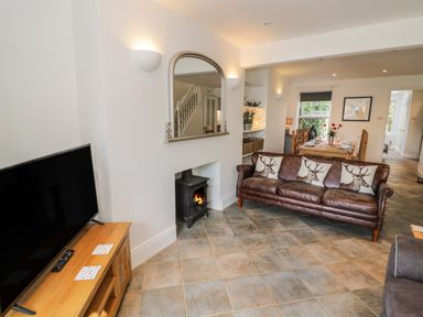 A living room with a leather sofa with deer cushions a wood stove a wall mirror a wooden TV stand with a television and a dining area with a table set for meals at Florence Villas in Worcester