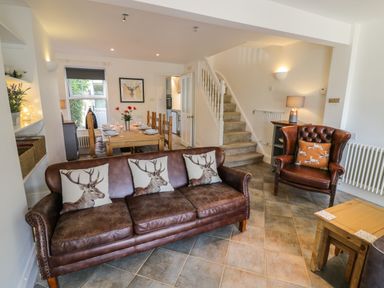 A living area with a leather sofa and armchair with deer cushions a dining table with chairs and a staircase at Florence Villas Worcester