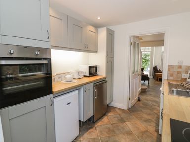 A kitchen with grey cabinets wooden countertops a built-in oven a white mini fridge a microwave toaster and kettle with a doorway leading to a living room at Florence Villas in Worcester