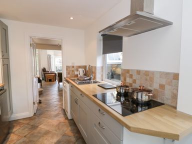 A narrow kitchen with stove pots sink and dishwasher with view into a living room at Florence Villas in Worcester