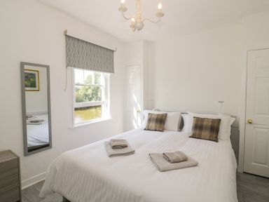 A bedroom with a double bed white bedding plaid pillows folded towels window with patterned blind and a wall mirror at Florence Villas in Worcester