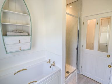 A bathroom with a bathtub with gold taps and a wall-mounted shelf with towels at Florence Villas in Worcester
