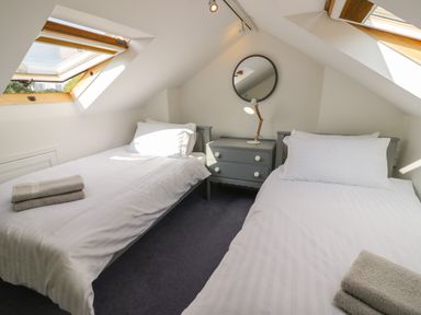 A bedroom with two single beds a nightstand with a lamp and a round mirror under skylight windows at Florence Villas in Worcester