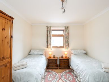 A bedroom with two single beds two wooden bedside tables a wooden wardrobe and a window with floral curtains at Penrallt Fawr in Rhosgadfan near Waunfawr