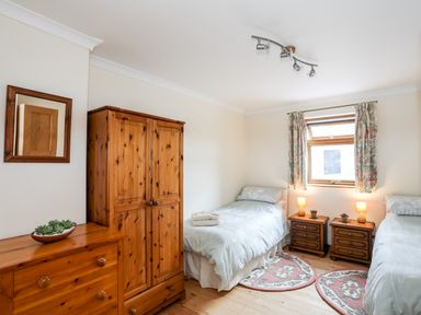 A bedroom with two single beds bedside tables wooden wardrobe and dresser at Penrallt Fawr Rhosgadfan near Waunfawr