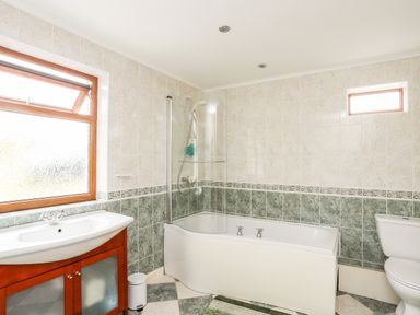 A bathroom with a bathtub shower combination a sink with vanity unit a toilet and two windows at Penrallt Fawr in Rhosgadfan near Waunfawr