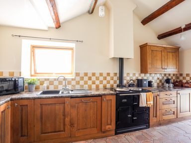 A kitchen with wooden cabinets a black stove a microwave and a window above the sink at Penrallt Fawr in Rhosgadfan near Waunfawr