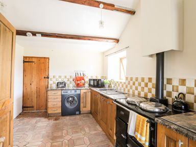 A kitchen with wooden cabinets a washing machine an oven toaster microwave and a kettle at Penrallt Fawr in Rhosgadfan near Waunfawr