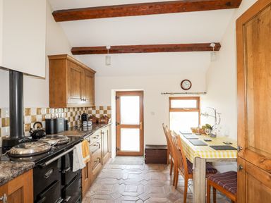 A kitchen with wooden cabinets and dining table with checkered tablecloth at Penrallt Fawr in Rhosgadfan near Waunfawr