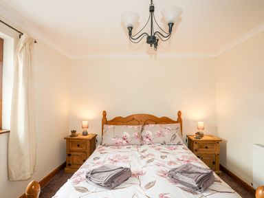 A bedroom with a wooden bed with floral bedding and two bedside tables with lamps and plants at Penrallt Fawr in Rhosgadfan near Waunfawr