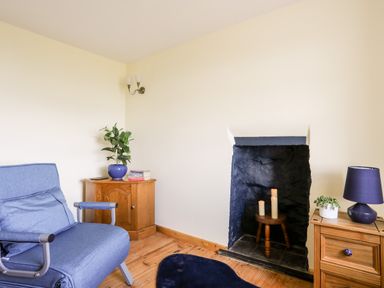 A room with a blue armchair wooden floor two wooden side tables a fireplace with candles and a lamp at Penrallt Fawr in Rhosgadfan near Waunfawr