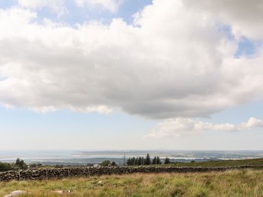 A rural landscape with a grassy field and stone wall under a cloudy sky