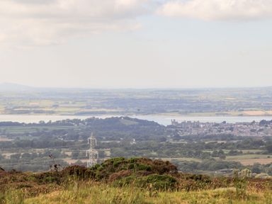 A rural landscape with fields trees and a distant town by a body of water with a power line in the foreground at Penrallt Fawr in Rhosgadfan near Waunfawr