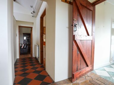 A hallway with red and black checkered floor tiles and a wooden door leading to adjacent rooms at Penrallt Fawr in Rhosgadfan near Waunfawr