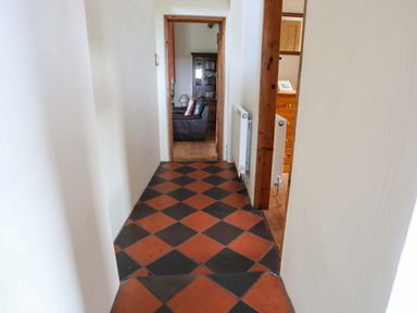 A hallway with black and red tiled floor leading to a room with a brown leather sofa and wooden furniture at Penrallt Fawr in Rhosgadfan near Waunfawr