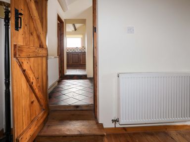 A wooden door open to a hallway with a tiled floor leading to a kitchen with wooden cabinets at Penrallt Fawr in Rhosgadfan near Waunfawr