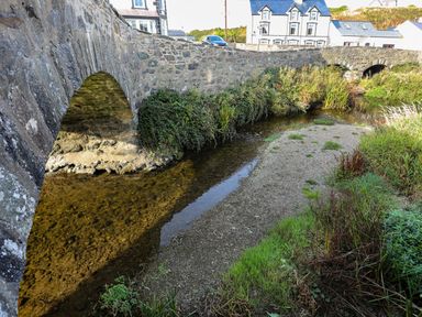 A bridge over a river with grass and buildings nearby at 4 Bryn Llan Aberdaron