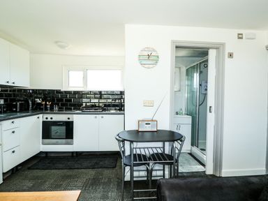 A kitchen with black tiled backsplash a black dining table with two chairs and a bathroom visible at 57 Cherry Park Chapel St Leonards