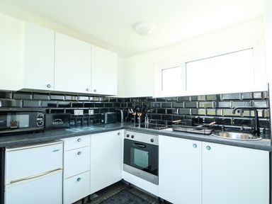 A kitchen with white cabinets black countertop and black tiled backsplash at 57 Cherry Park in Chapel St Leonards