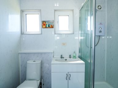 A bathroom with a toilet sink cabinet shower enclosure and two small windows at 57 Cherry Park in Chapel St Leonards