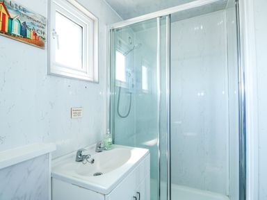 A bathroom with a shower enclosure a sink a window and a wall decoration at 57 Cherry Park in Chapel St Leonards