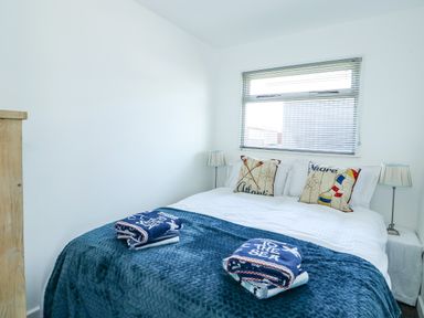 A bedroom with a bed covered in blue and white bedding and two pillows with coastal designs at 57 Cherry Park in Chapel St Leonards