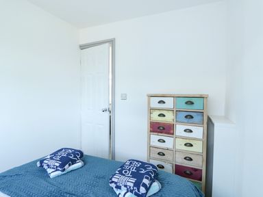 A bedroom with a partially open white door a bed with folded towels and a multicolored drawer unit at 57 Cherry Park in Chapel St Leonards