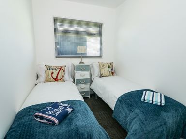 A bedroom with two single beds with pillows and blankets a bedside table with a lamp below a window at 57 Cherry Park in Chapel St Leonards