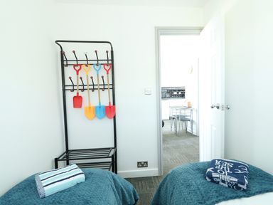 A bedroom with two beds covered with blue blankets and towels hanging on a black metal rack at 57 Cherry Park in Chapel St Leonards