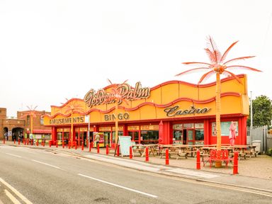 A street view of a colorful amusement arcade with bingo and casino signs and outdoor seating at 57 Cherry Park in Chapel St Leonards